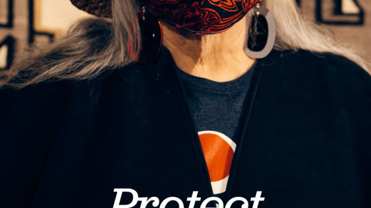 An Elder in a cedar hat and a red masks looks at the camera behind text: Protect Our Future Generations.